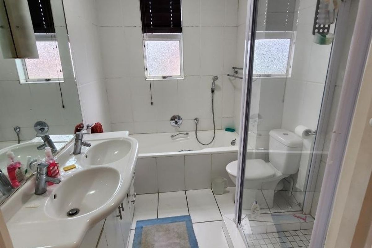 A functional bathroom featuring a double vanity, built-in bathtub, separate shower enclosure, and toilet with tiled finishes throughout.