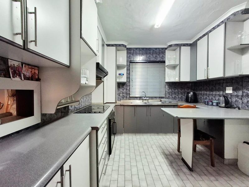 Functional kitchen featuring built-in cabinetry, laminate countertops, an electric hob, oven, extractor fan, and tiled finishes throughout.