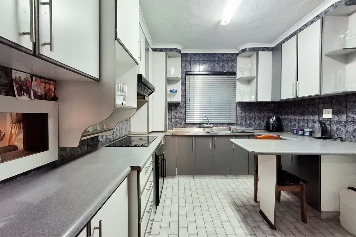 Functional kitchen featuring built-in cabinetry, laminate countertops, an electric hob, oven, extractor fan, and tiled finishes throughout.