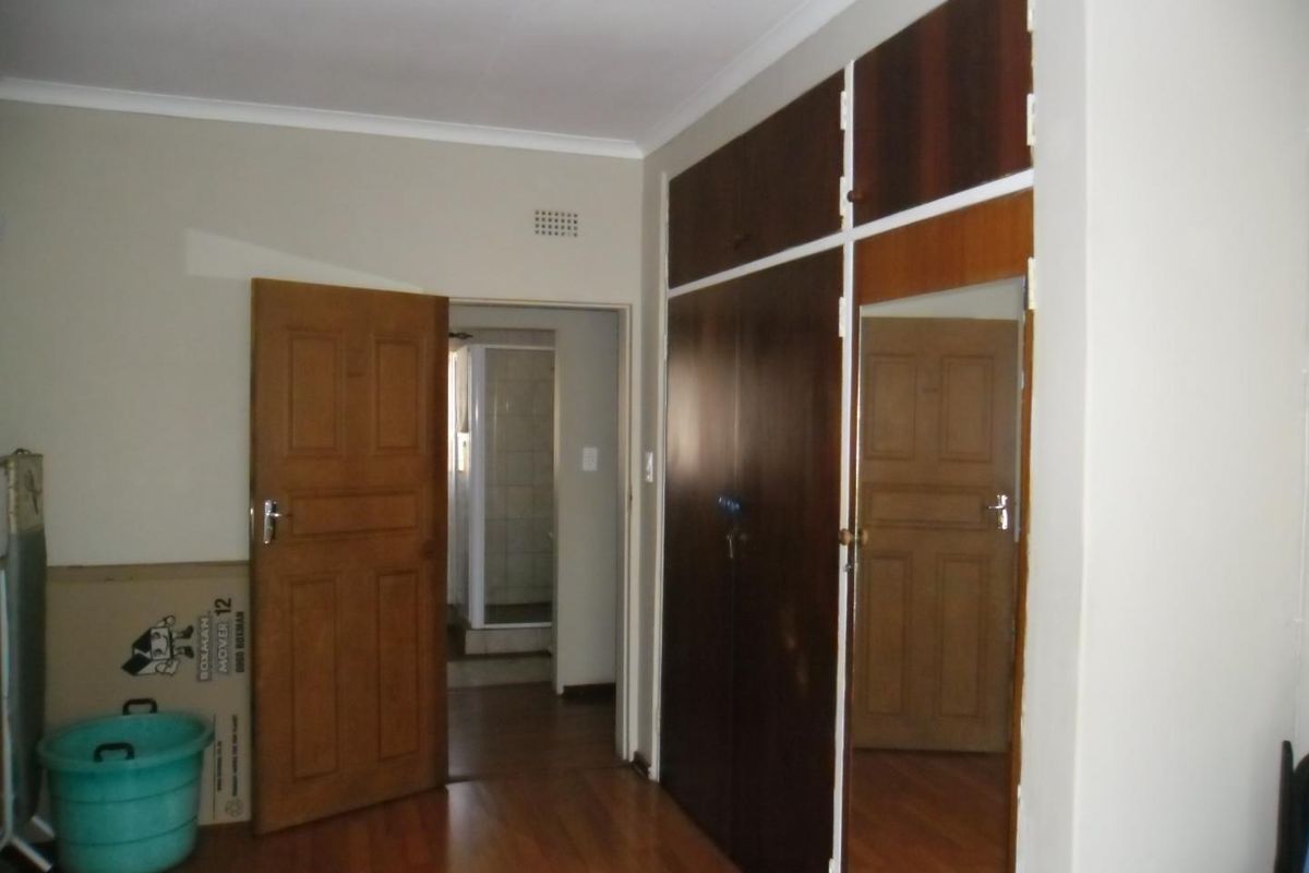 A bedroom featuring laminate flooring, built-in cupboards with a mirrored panel, and direct access to an adjacent bathroom.
