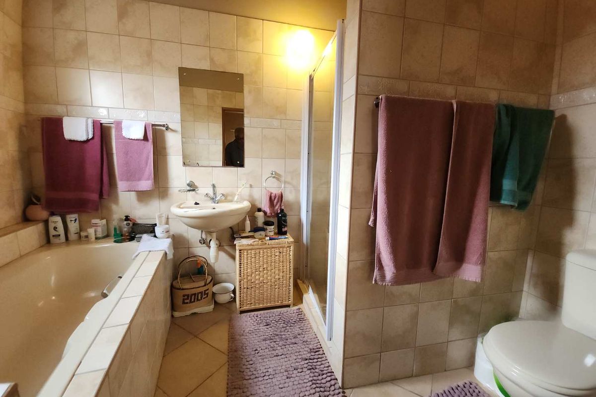 A functional bathroom featuring a built-in bathtub, a separate shower enclosure, a pedestal sink, and a toilet with neutral wall and floor tiling.