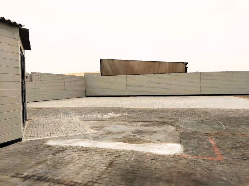 A spacious industrial yard featuring extensive paved surfaces enclosed by a perimeter boundary wall and a corrugated metal structure.