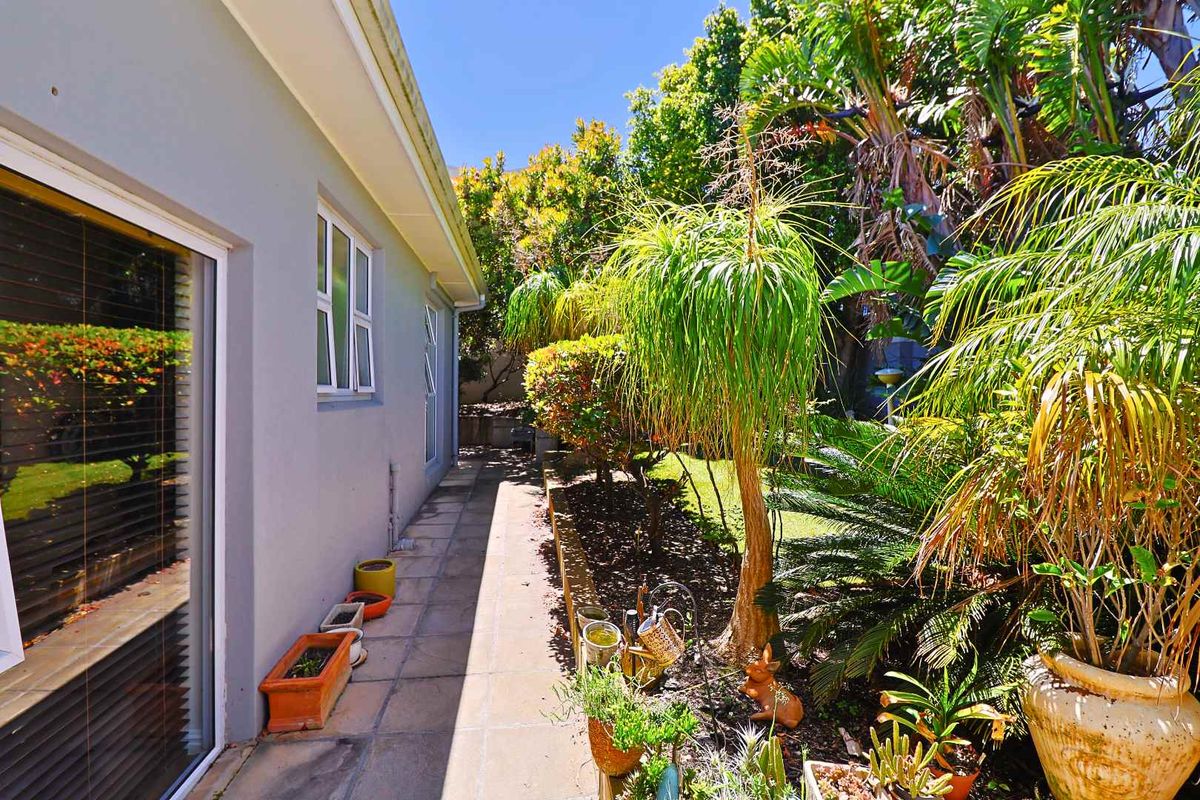 A side garden pathway featuring a paved walkway, retaining wall, and established landscaping alongside the exterior wall of the house.