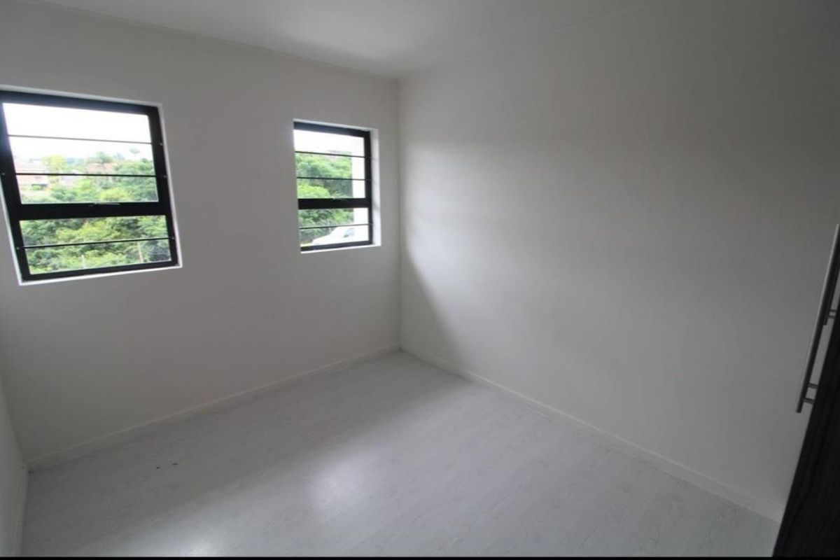A bright, empty bedroom featuring neutral walls, laminate flooring, and two windows with security bars overlooking greenery.