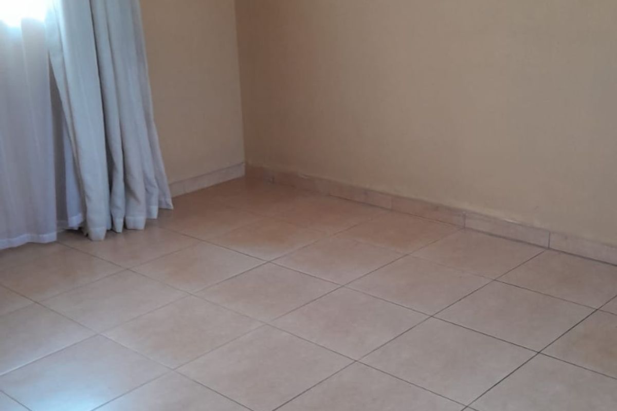 A clean, empty bedroom featuring neutral wall paint, tiled flooring, and simple window treatments, offering a blank canvas for personalization.