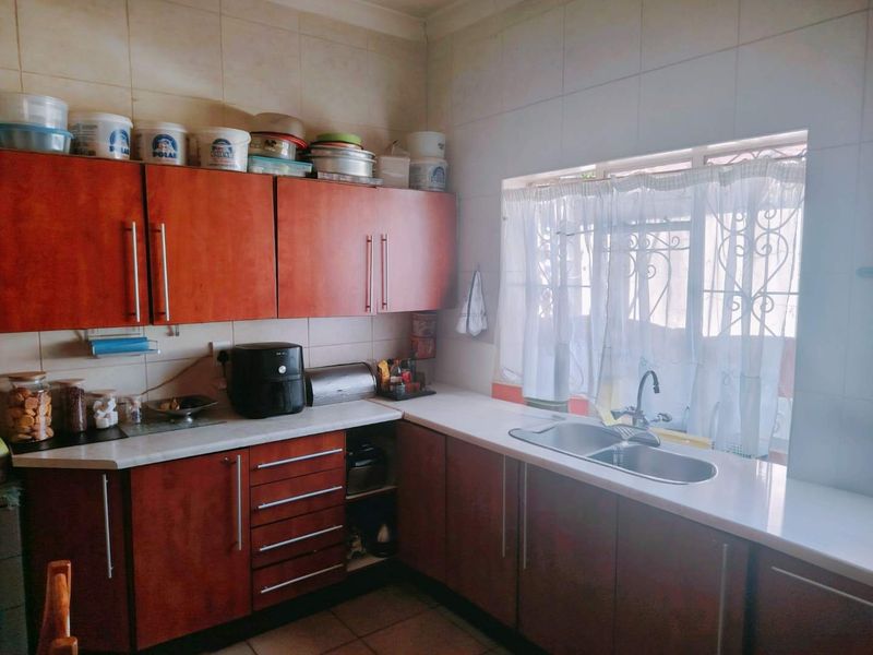 A functional kitchen featuring wood-look laminate cabinetry, a double bowl stainless steel sink, tiled backsplash, and tiled flooring with natural light from the window.
