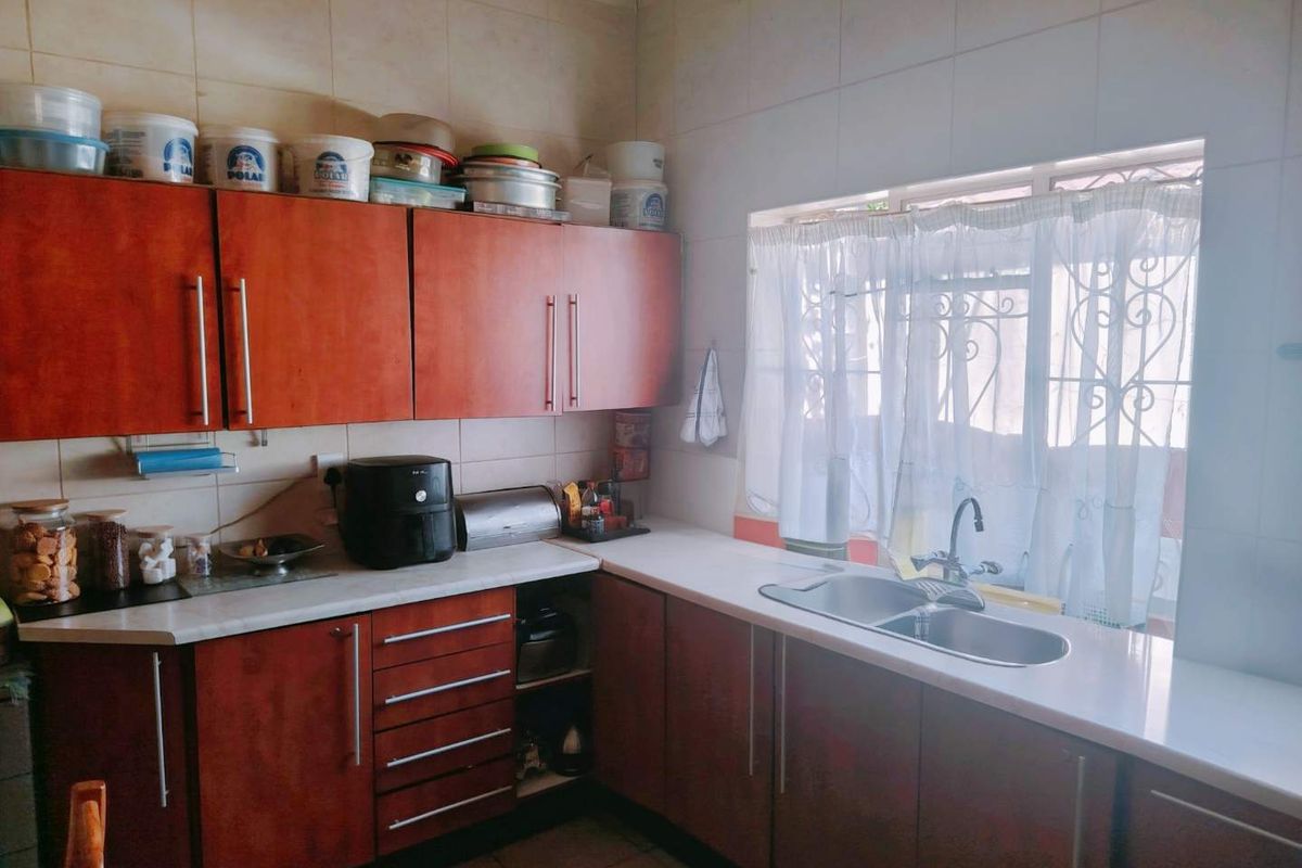 A functional kitchen featuring wood-look laminate cabinetry, a double bowl stainless steel sink, tiled backsplash, and tiled flooring with natural light from the window.