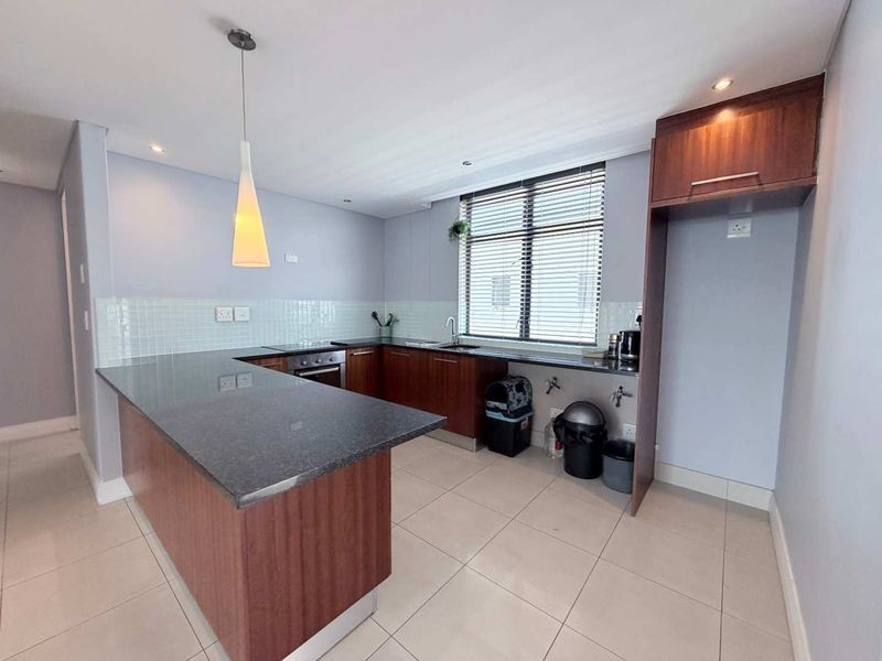 Modern kitchen featuring dark wood cabinetry, granite countertops, built-in oven, hob, and a tiled backsplash, offering a clean and functional workspace.