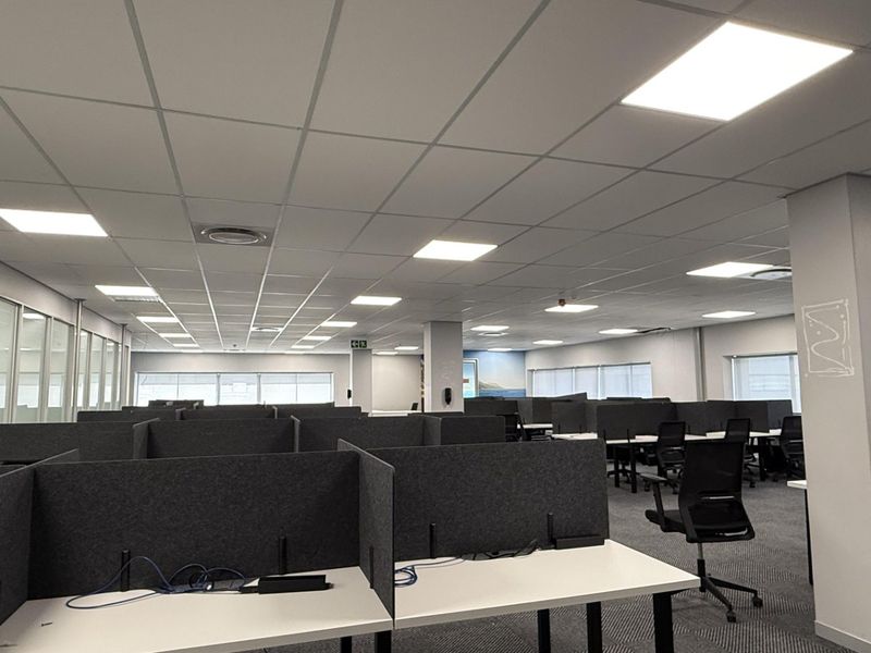 Open-plan office space featuring modular workstations with privacy partitions, suspended ceilings with recessed LED lighting, and glass-walled meeting rooms.