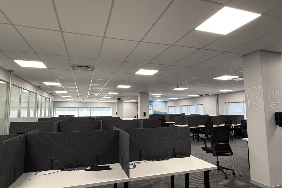 Open-plan office space featuring modular workstations with privacy partitions, suspended ceilings with recessed LED lighting, and glass-walled meeting rooms.