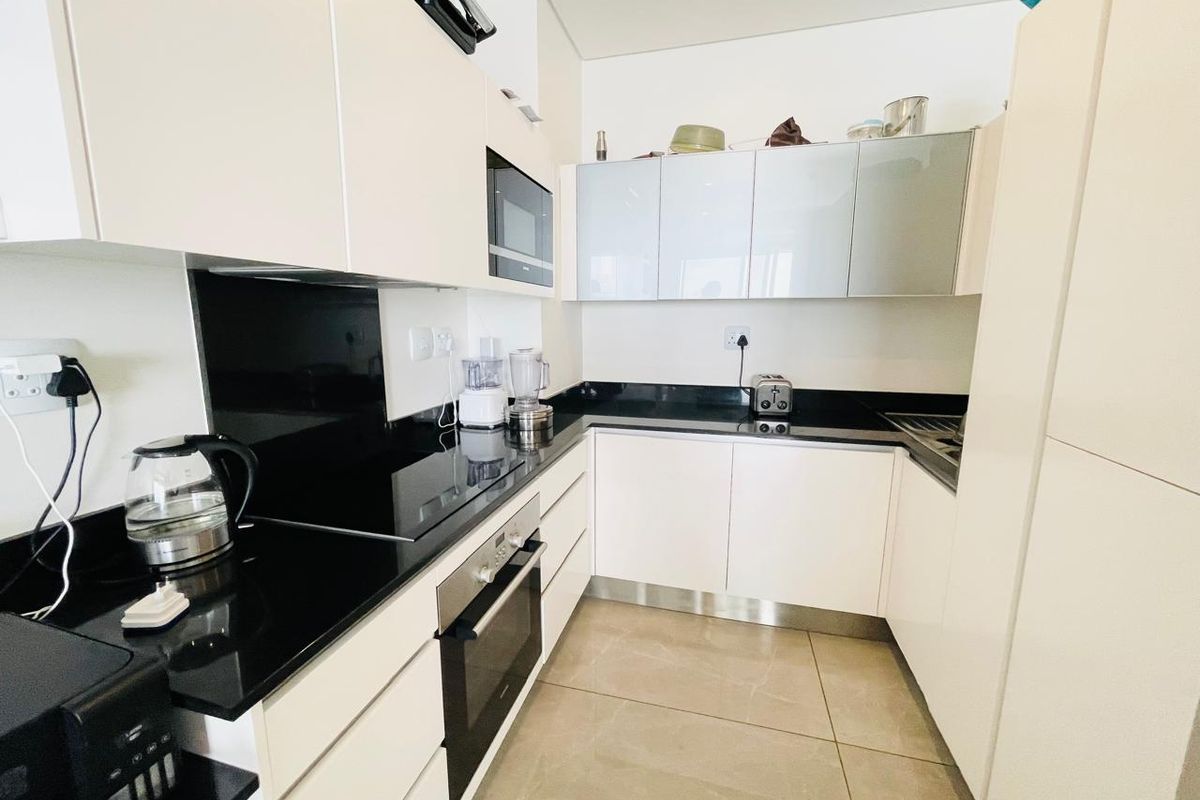 Modern kitchen featuring sleek white gloss cabinetry, black granite countertops, integrated oven, hob, and microwave with large format floor tiles.