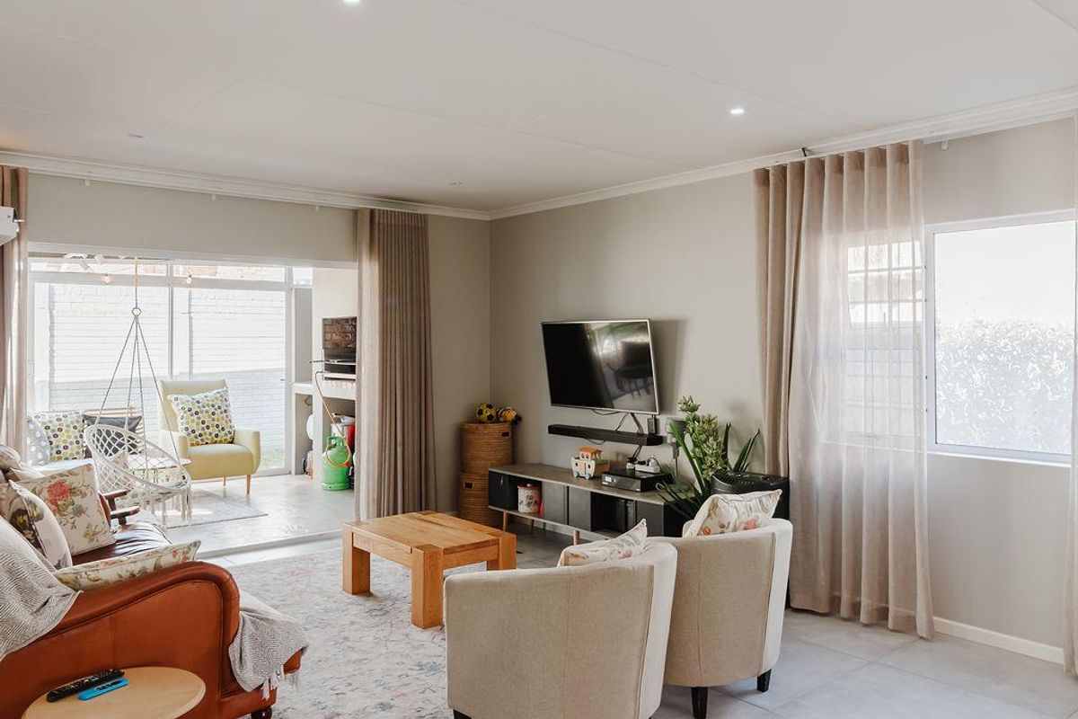 Bright and spacious living room featuring large sliding glass doors that open onto a covered patio, with neutral tiled flooring and recessed ceiling lighting.
