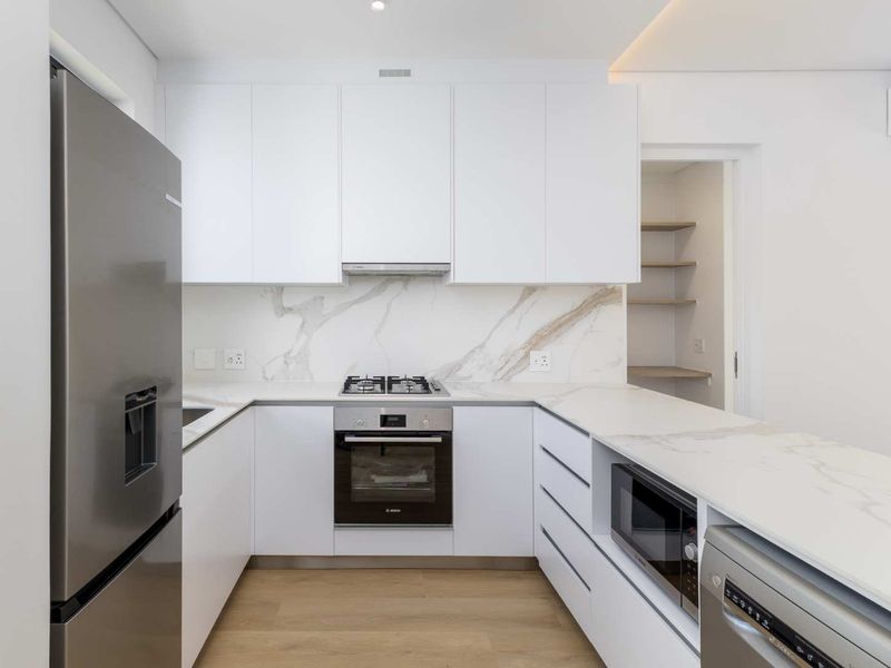 Modern kitchen featuring white cabinetry, marble-look stone countertops and backsplash, built-in oven, gas hob, and an adjacent pantry area.