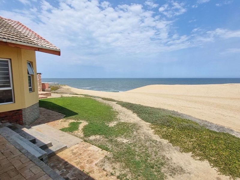 Rear exterior view of the property featuring brick paving, concrete steps, and direct access to the coastal dunes and ocean.