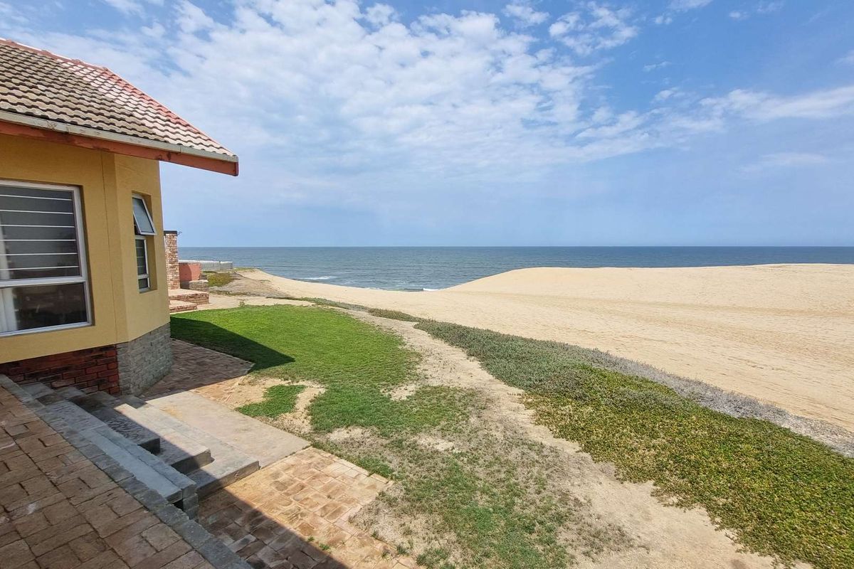 Rear exterior view of the property featuring brick paving, concrete steps, and direct access to the coastal dunes and ocean.
