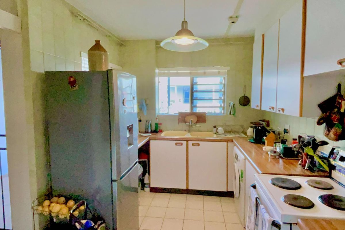 A dated kitchen featuring original cabinetry, tiled flooring, and a functional layout with built-in stove and sink area.