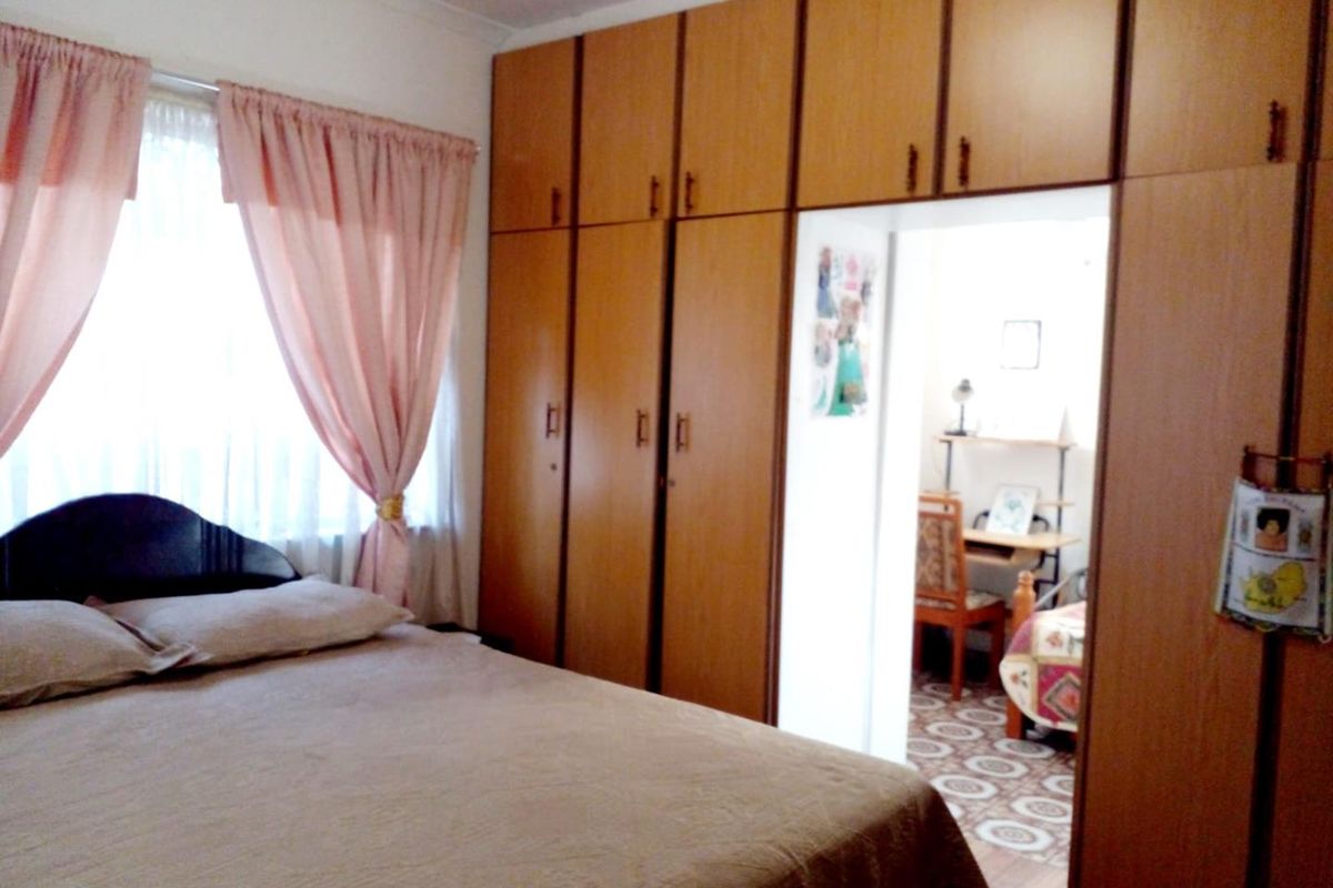 A bedroom featuring floor-to-ceiling built-in wooden cupboards and a window with curtains, providing functional storage and natural light.