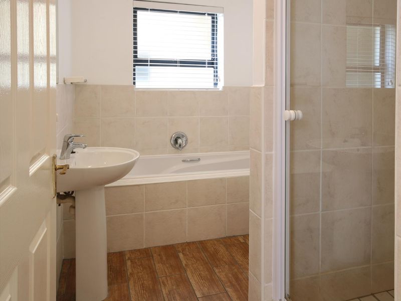 A clean, functional bathroom featuring a pedestal basin, built-in bathtub, and a separate shower enclosure with neutral wall tiling and wood-look floor tiles.