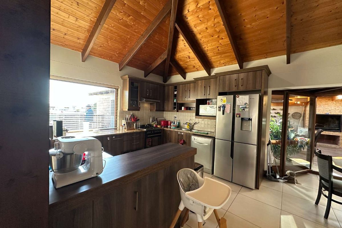 A spacious kitchen featuring dark wood cabinetry, a breakfast bar, tiled flooring, and a vaulted timber-beamed ceiling, offering a warm and functional cooking space.