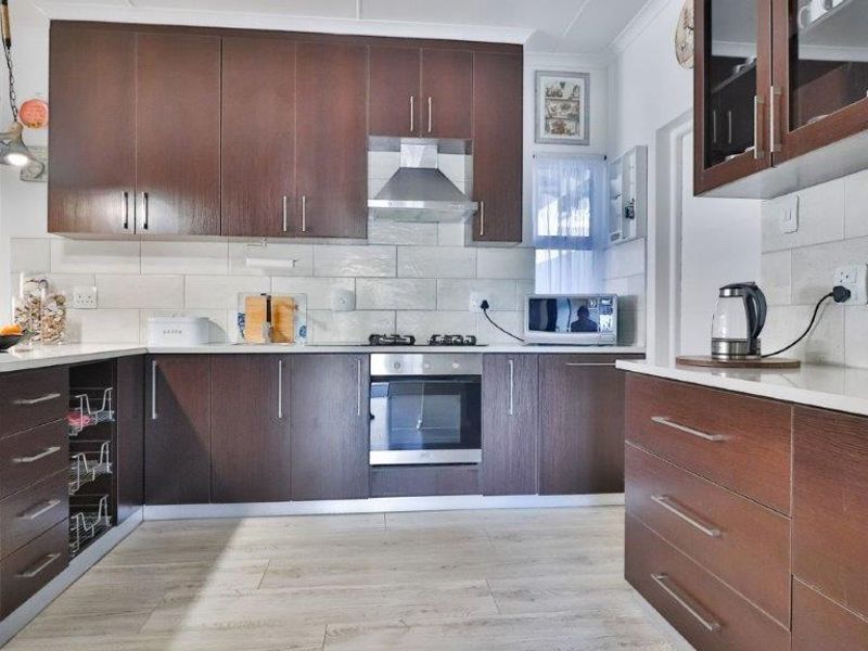 Modern kitchen featuring dark wood cabinetry, stainless steel appliances, subway tile backsplash, and light-toned laminate flooring.