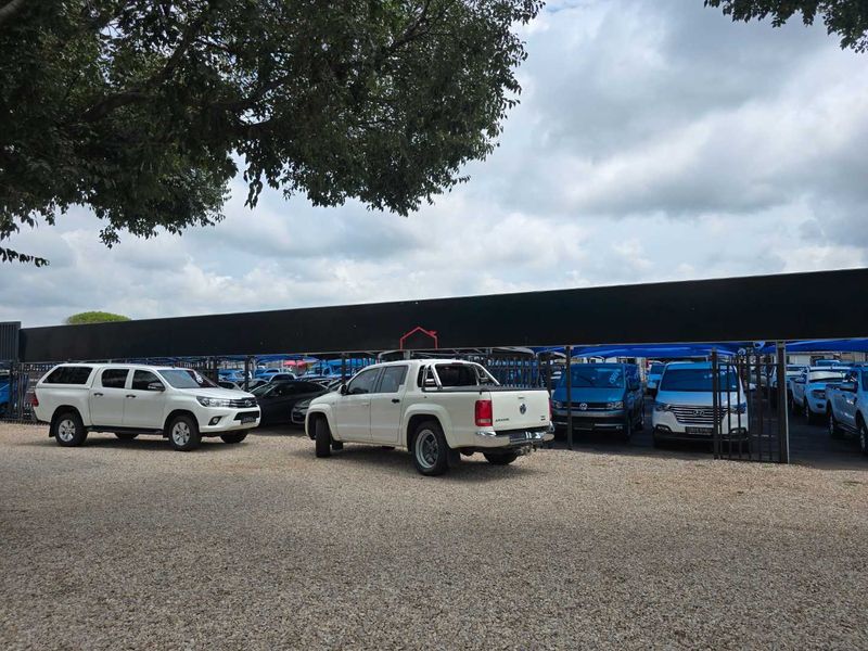 A commercial vehicle display area featuring a gravel surface and a large shade cloth canopy structure for vehicle protection.