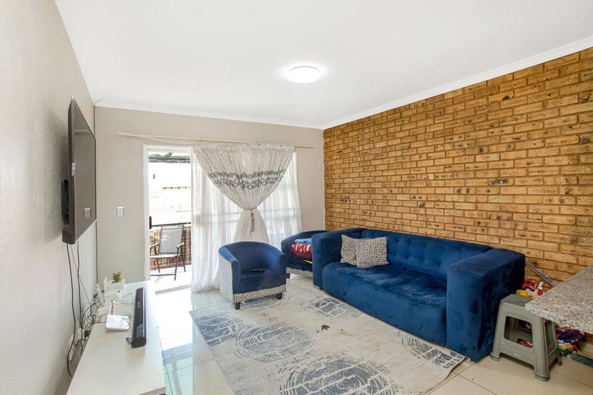 A living room featuring a prominent exposed brick feature wall, tiled flooring, and sliding glass door access to an outdoor patio area.