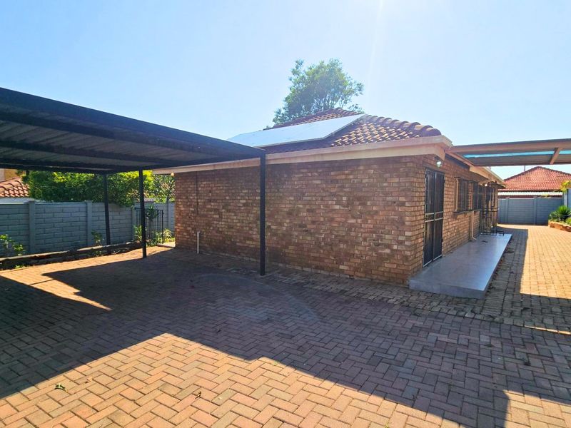 Rear view of a face brick house featuring a paved driveway, carport, and solar panels installed on the tiled roof.