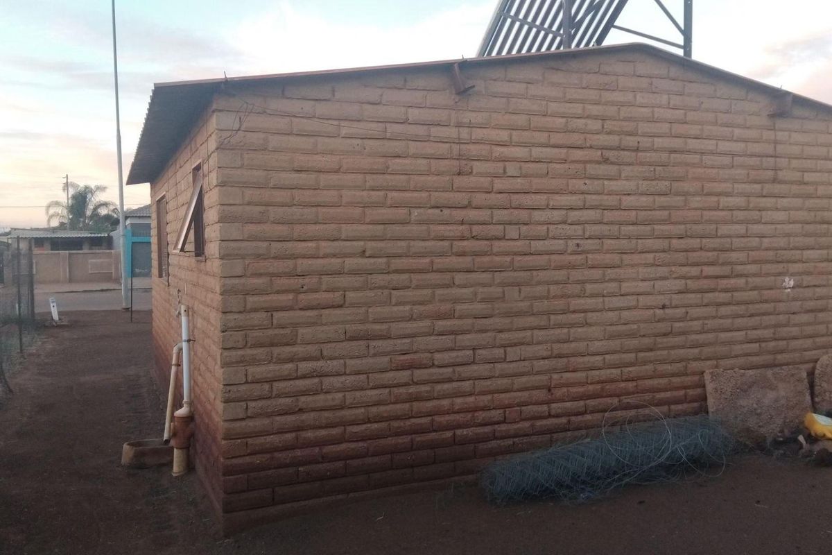 Exterior view of a simple brick structure featuring a solar water heating system mounted on the roof.