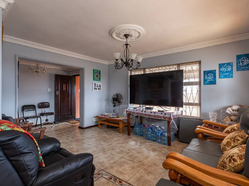 A spacious living room featuring tiled flooring, decorative ceiling cornices, and a central ceiling rose, providing a functional and well-lit living area.