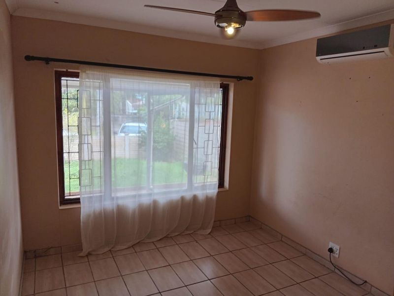 A vacant bedroom featuring tiled flooring, a ceiling fan, and a wall-mounted air conditioning unit, offering a blank canvas for personalization.