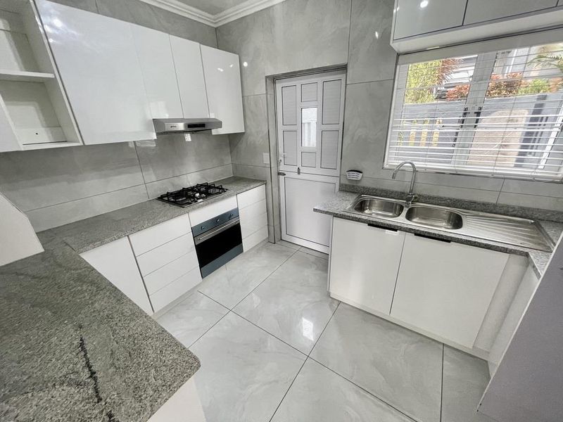 Modern kitchen featuring granite countertops, built-in gas hob, oven, extractor fan, and double bowl sink with sleek white cabinetry and tiled finishes.