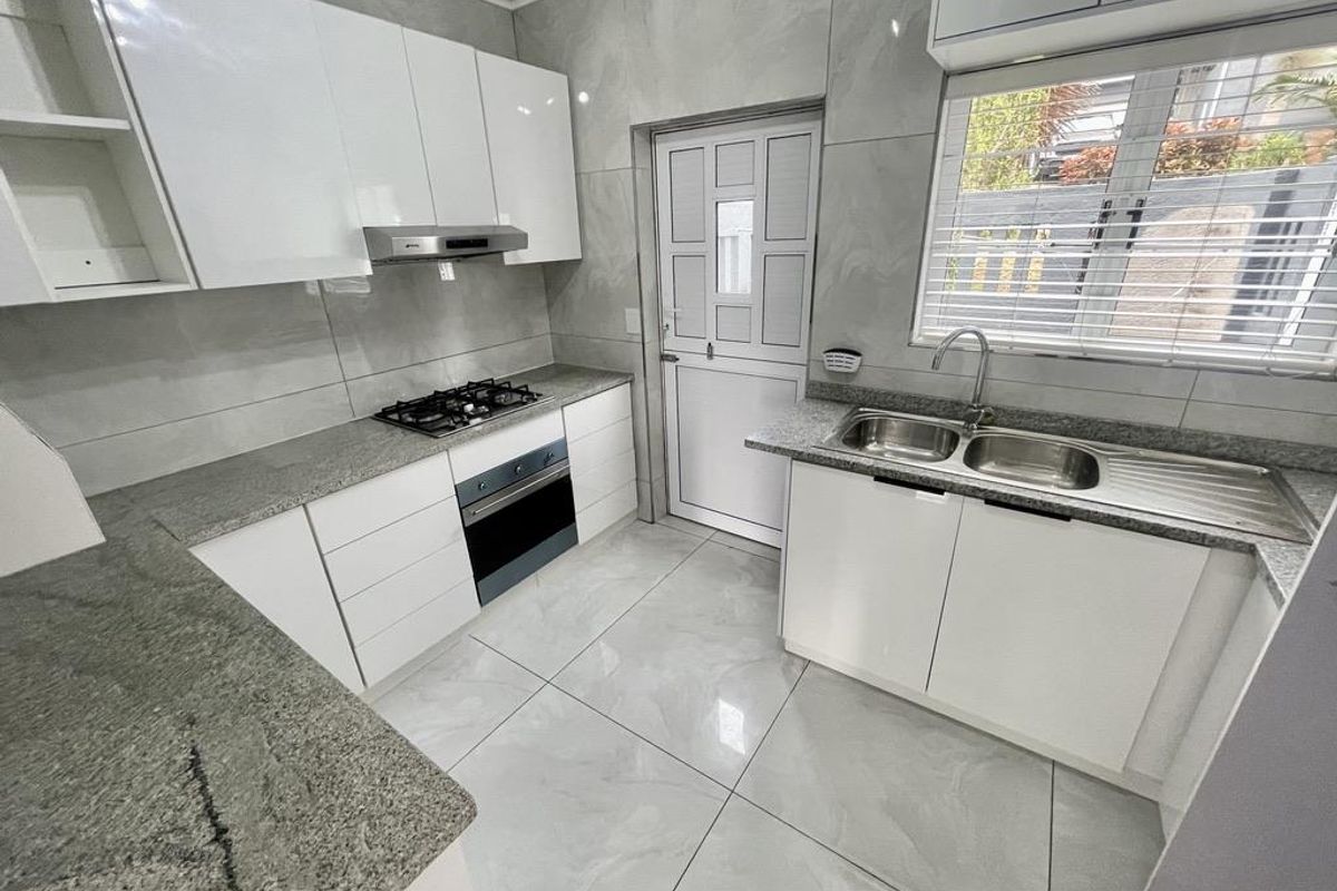 Modern kitchen featuring granite countertops, built-in gas hob, oven, extractor fan, and double bowl sink with sleek white cabinetry and tiled finishes.