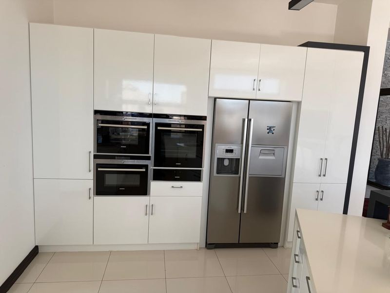 Modern kitchen featuring high-gloss white cabinetry, integrated stainless steel appliances, built-in oven and microwave, and sleek tiled flooring.