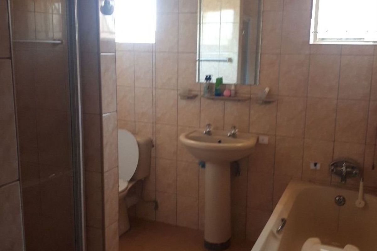 A functional bathroom featuring a pedestal sink, a built-in bathtub, and a separate glass-enclosed shower stall with full-height wall tiling.