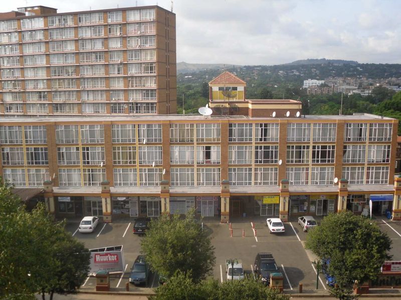 Exterior view of a multi-story apartment building featuring ground-level retail spaces and a paved parking area.