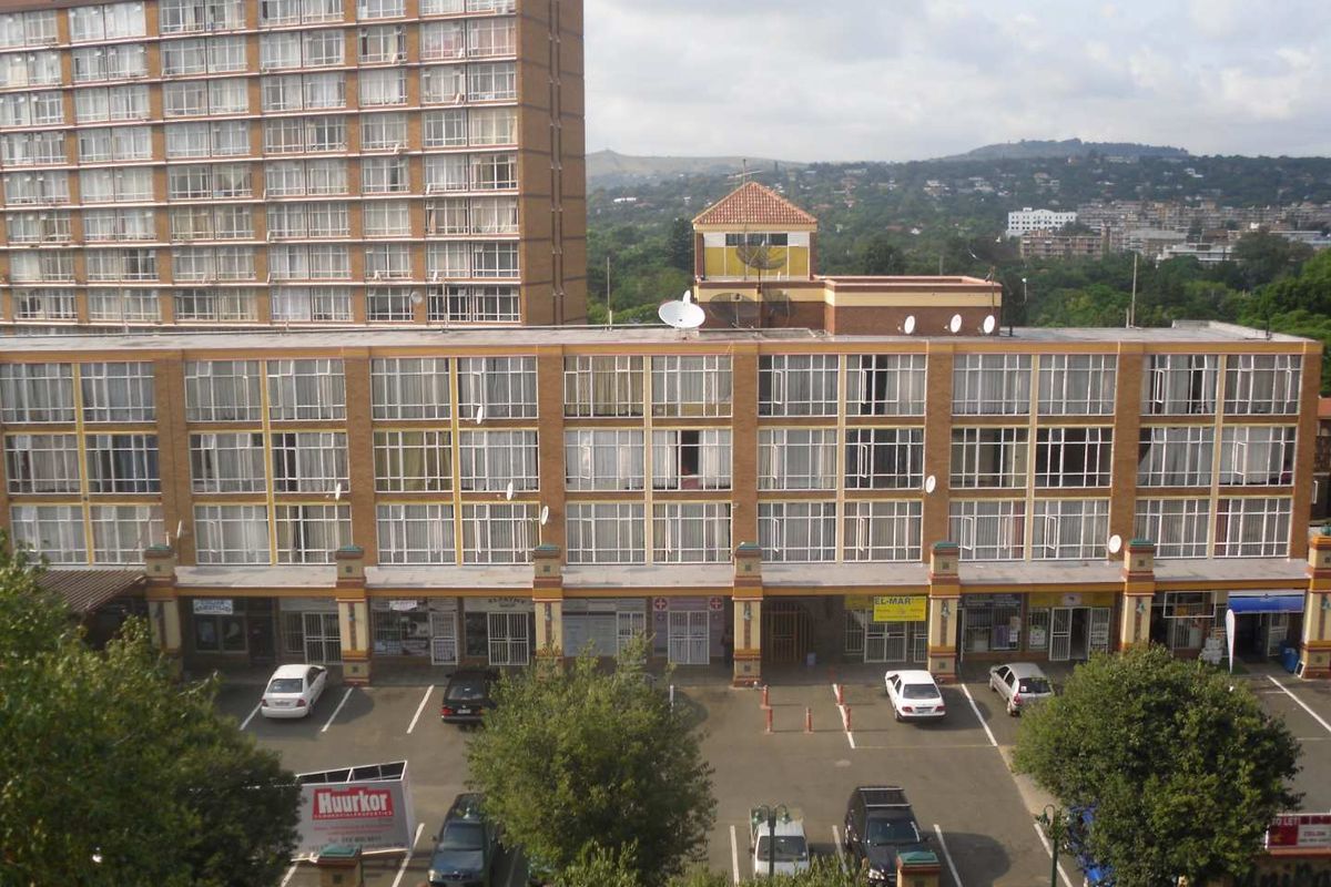 Exterior view of a multi-story apartment building featuring ground-level retail spaces and a paved parking area.