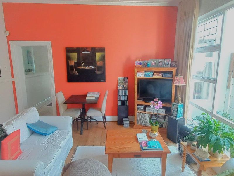 A bright living room featuring timber flooring and a large window with security bars, providing natural light and a view of the exterior.