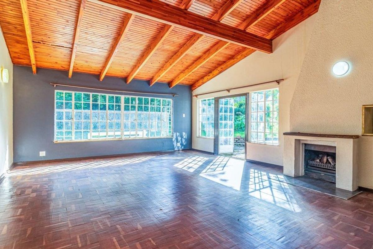 Spacious living room featuring high exposed timber beam ceilings, classic parquet flooring, and a built-in fireplace with direct access to the garden.