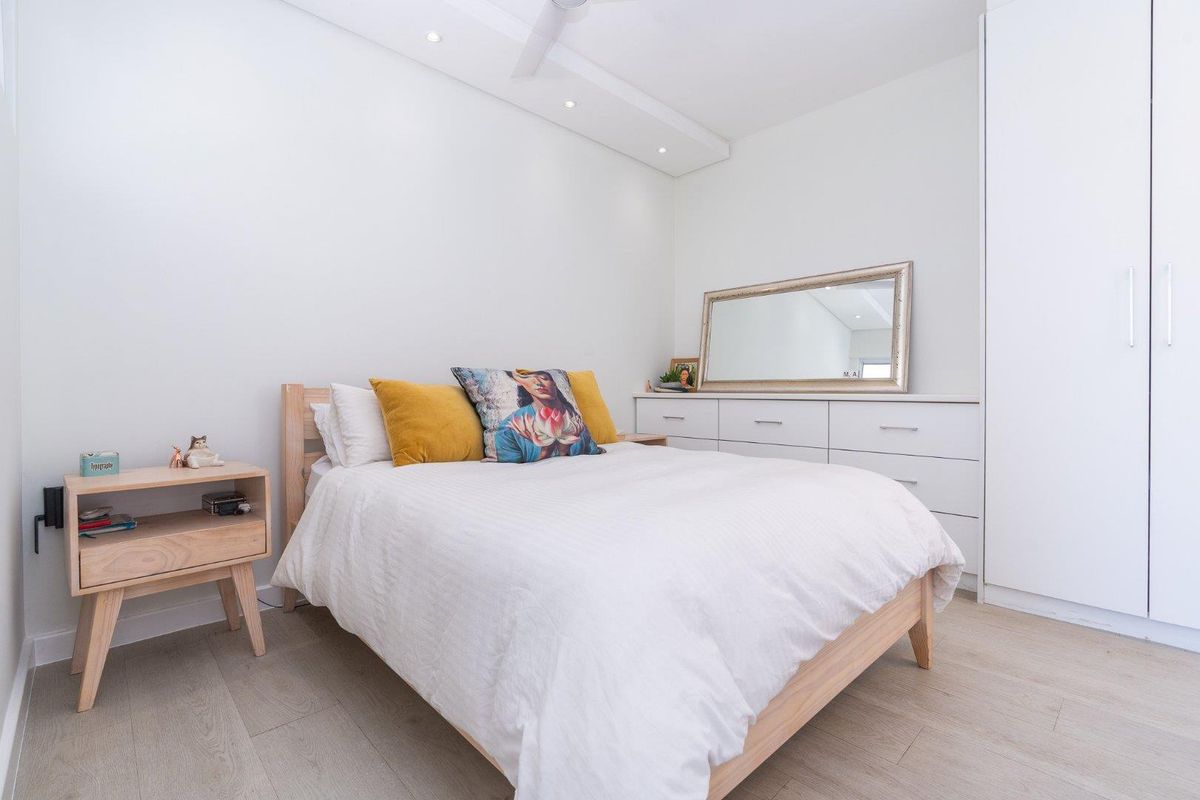 A bright and modern bedroom featuring light laminate flooring, recessed ceiling lighting, and a spacious built-in wardrobe.