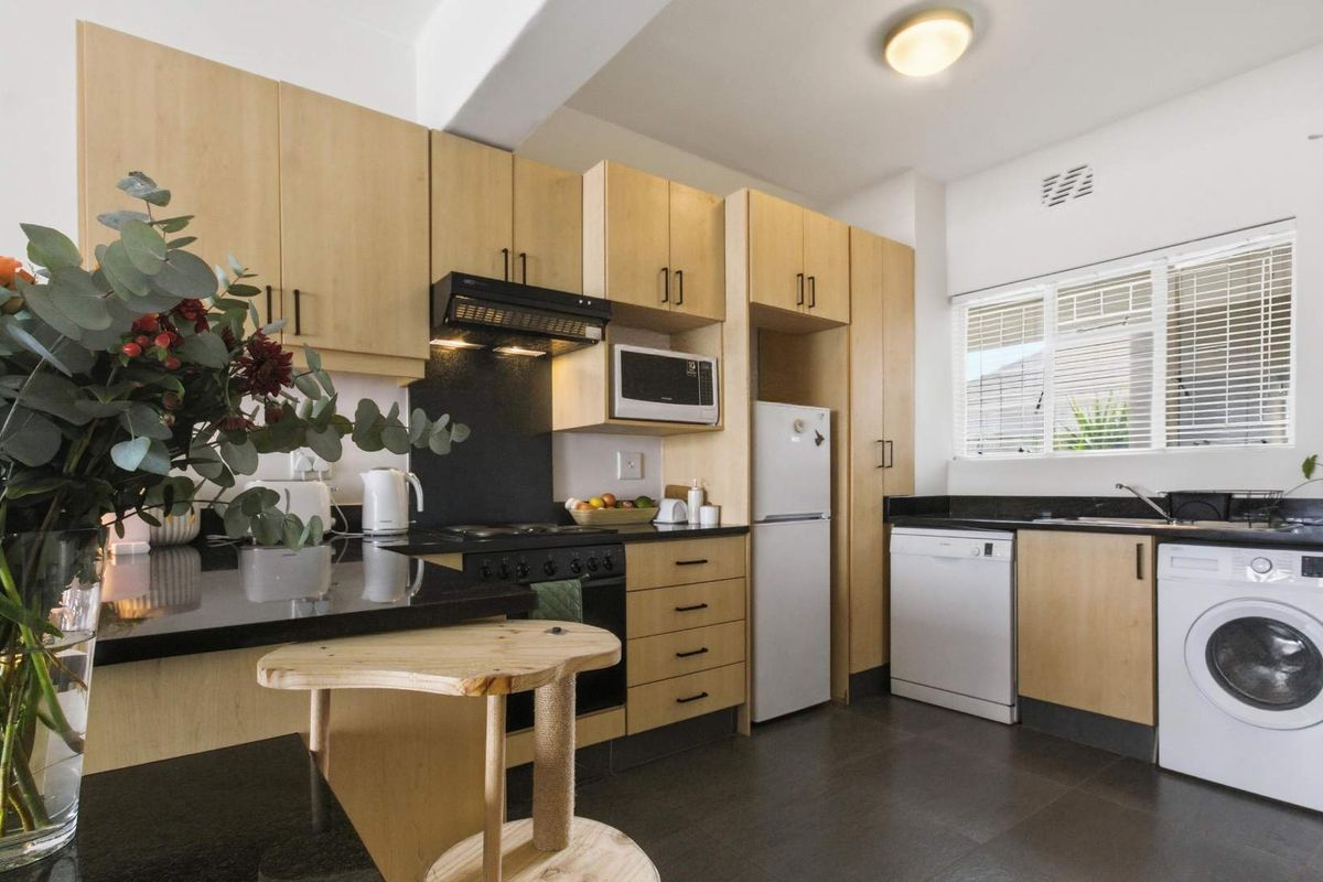 A functional kitchen featuring light-wood cabinetry, black granite countertops, and integrated spaces for a dishwasher and washing machine.