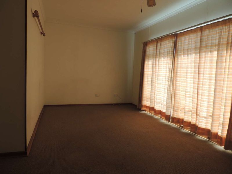 An empty living room featuring carpet flooring, a ceiling fan, and large windows with curtains, offering a blank canvas for potential interior updates.