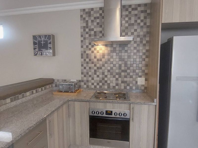 A functional kitchen featuring granite countertops, mosaic tile backsplash, built-in oven with electric hob, stainless steel extractor fan, and light wood-finish cabinetry.