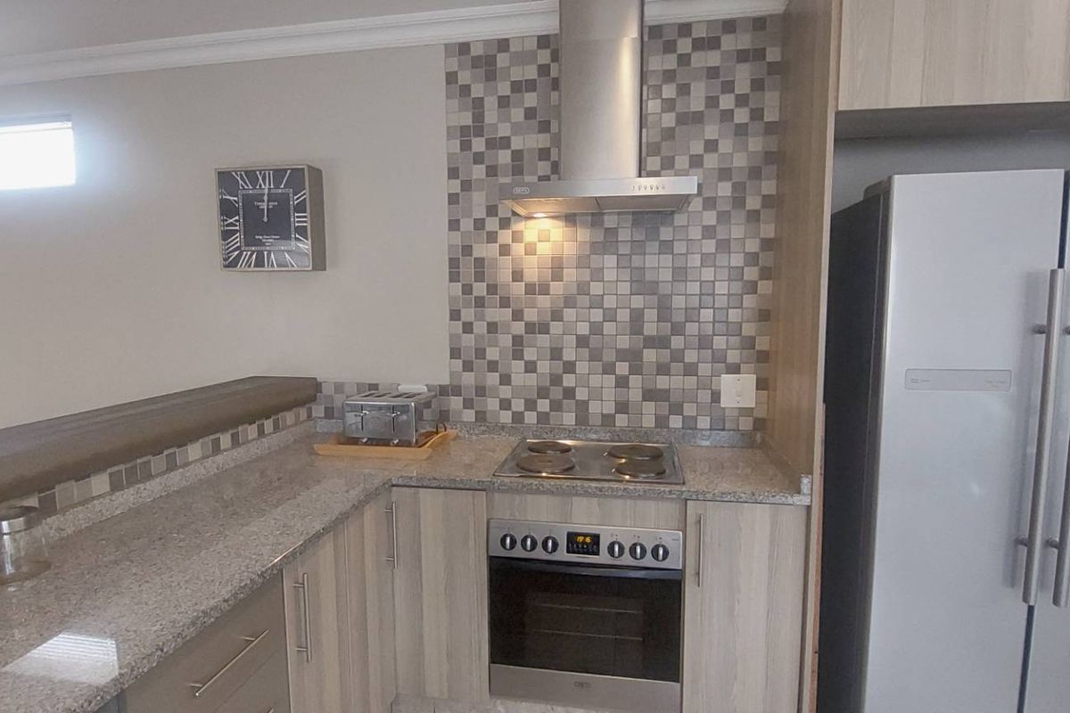 A functional kitchen featuring granite countertops, mosaic tile backsplash, built-in oven with electric hob, stainless steel extractor fan, and light wood-finish cabinetry.