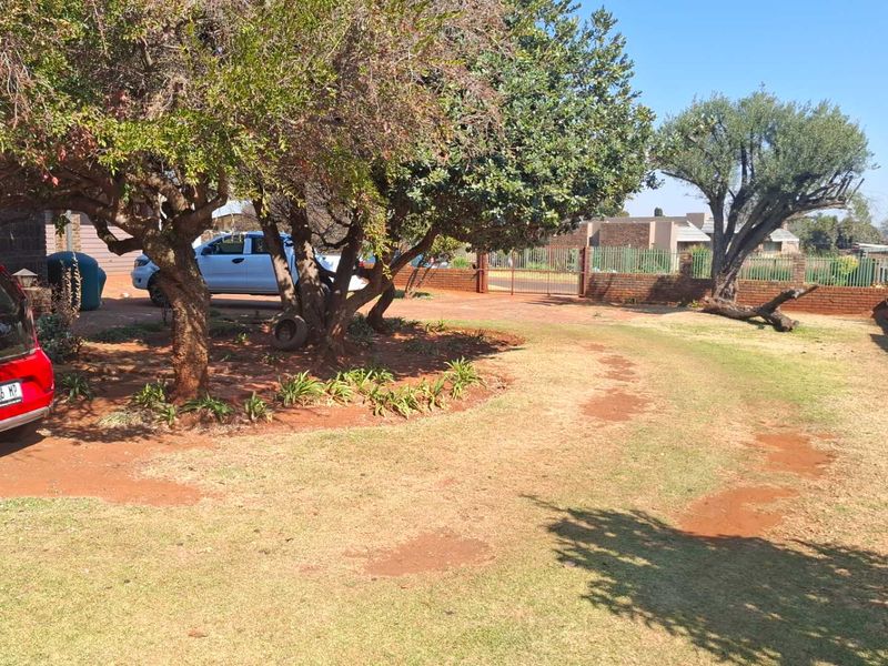 A spacious front yard area featuring mature trees, a brick boundary wall, and a metal gate entrance.