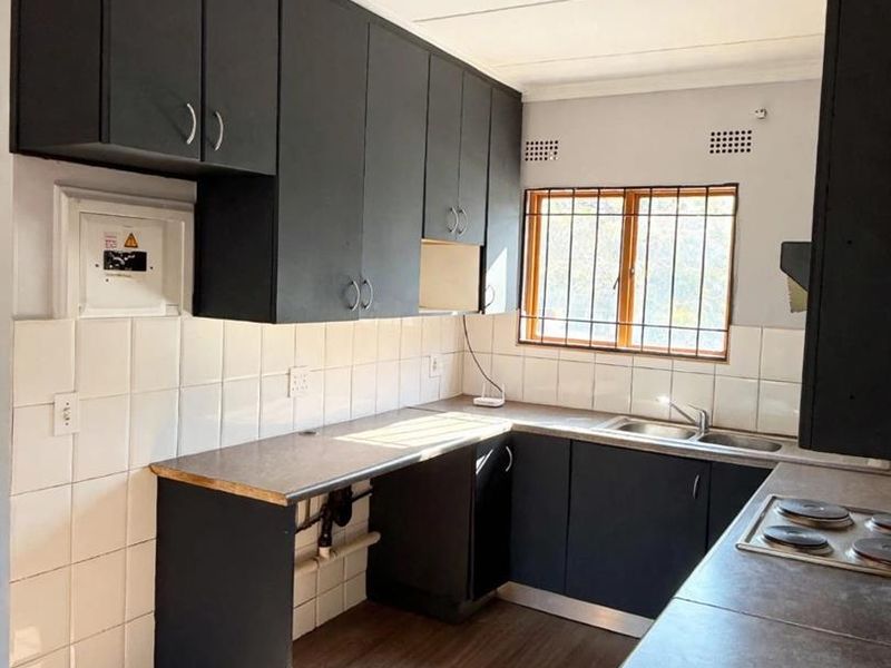 A functional kitchen featuring dark cabinetry, laminate countertops, a double sink, and an electric hob, with tiled backsplash and vinyl flooring throughout.
