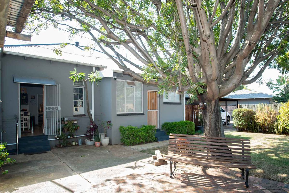 Rear exterior view of the house featuring a paved patio area, mature tree, and direct access to the home through security gates.