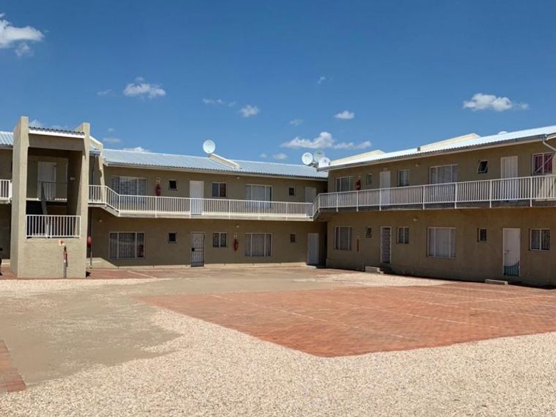 Exterior view of a multi-unit townhouse complex featuring a shared paved courtyard, gravel driveway, and upper-level balcony access.