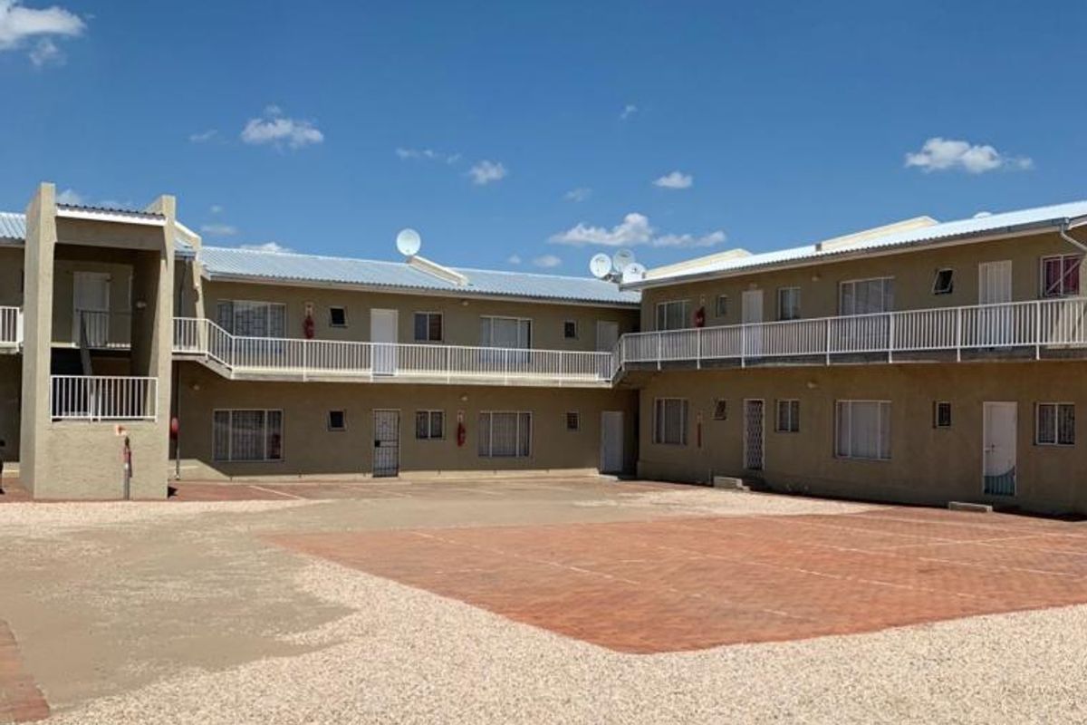 Exterior view of a multi-unit townhouse complex featuring a shared paved courtyard, gravel driveway, and upper-level balcony access.