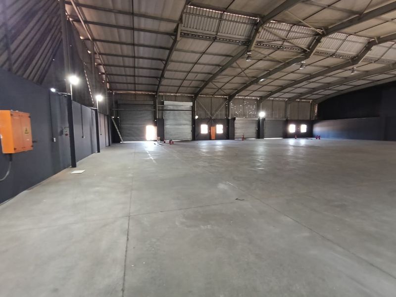 Spacious industrial warehouse featuring concrete flooring, high ceilings with steel portal frame construction, multiple roller shutter doors, and functional high bay lighting.