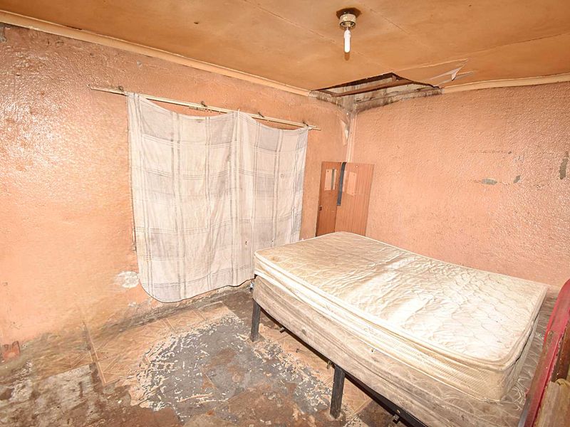 A bedroom in poor condition requiring significant renovation, featuring damaged ceiling panels, worn wall finishes, and degraded flooring.